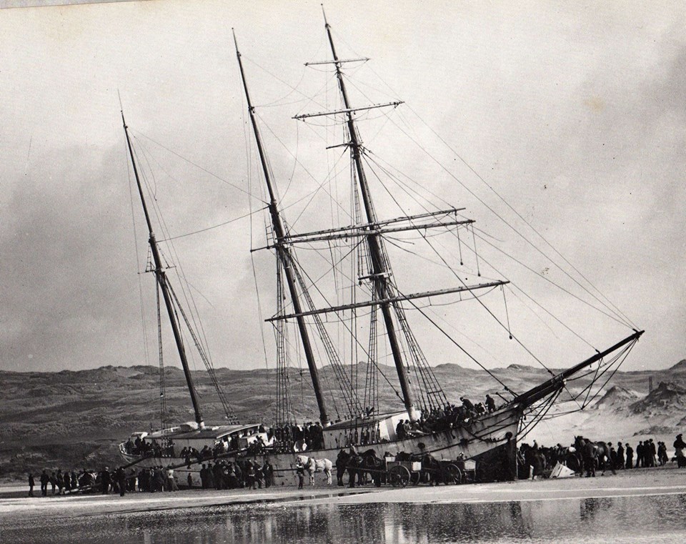 Crowd of people on beach looking at wrecked ship.