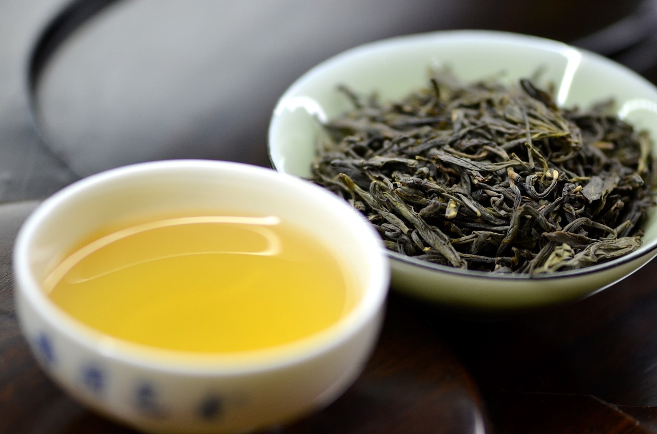 small cup of tea next to dish of dried loose tea leaves