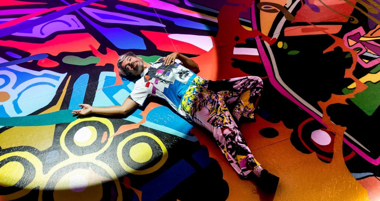 man in brightly patterned clothes lays on bright graffitied floor