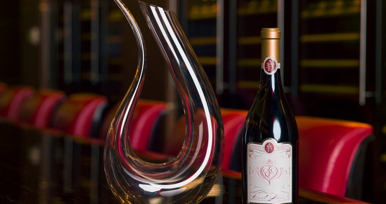 a bottle of red wine sits on a table with a curved decanter sitting beside it