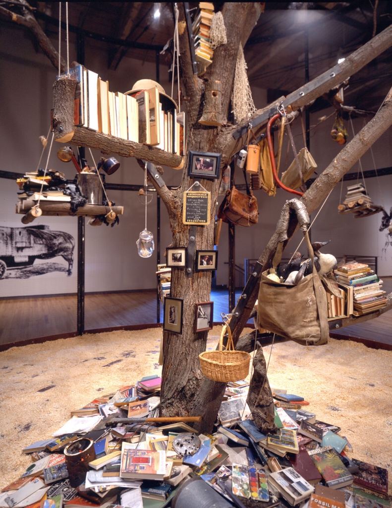 A tree indoors set up as a library with books hanging on shelves made of logs