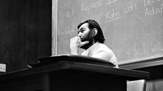 Black and white photo of Julio Cortazar sitting in front of a chalkboard.
