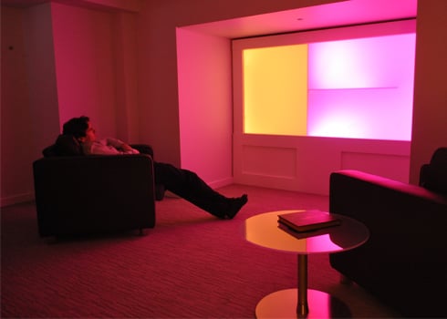 man sits reclined in an armchair in a pink lit room