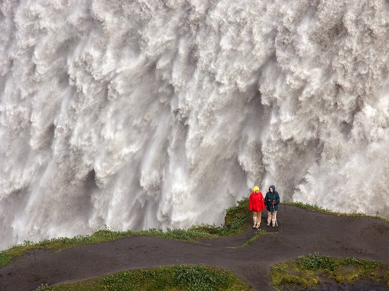 two people stand in front of Dettifoss waterfall in Iceland
