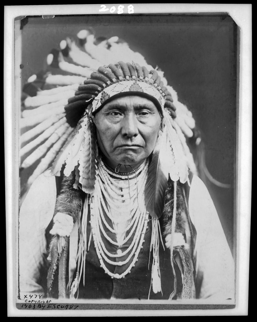Native American chief with large head dress covered in feathers and wearing a lot of necklaces