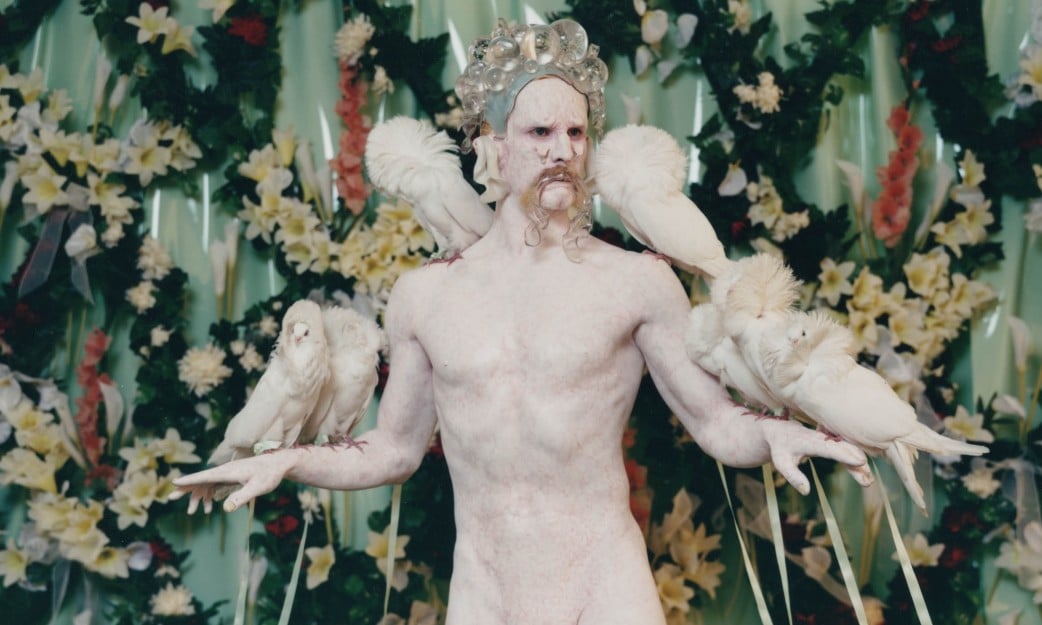 Man painted to look like statue, holding birds 