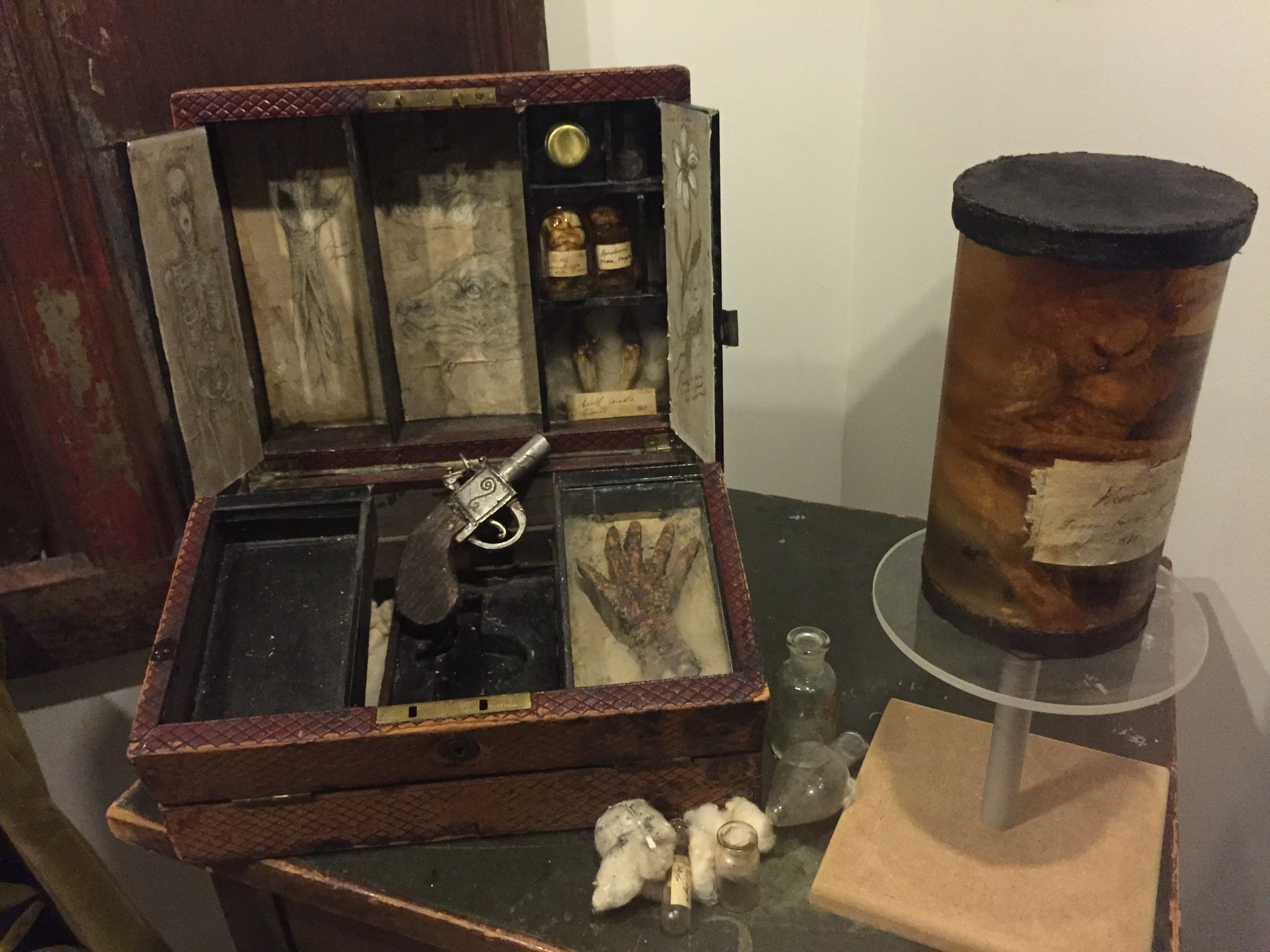 A box with many compartments, a small pistol, and a jar with brown liquid.