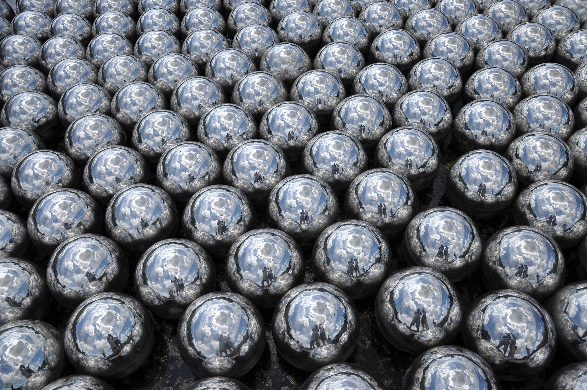 A close up of silver metal marbles with a reflection of a couple in each of them