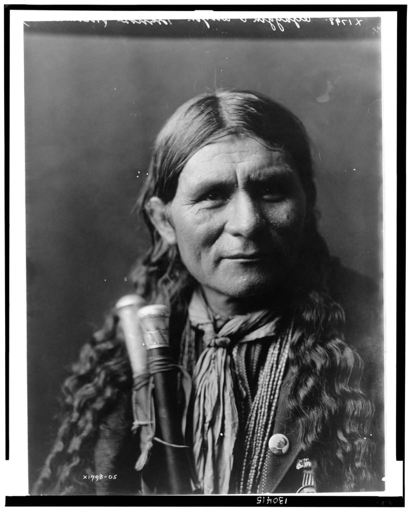 Native American chief with long hair and weapons strapped to his body in traditional clothing