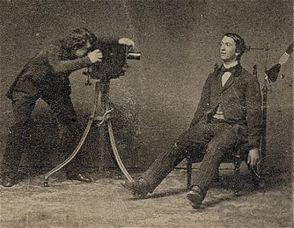 A photographer photographs a corpse in a seated position