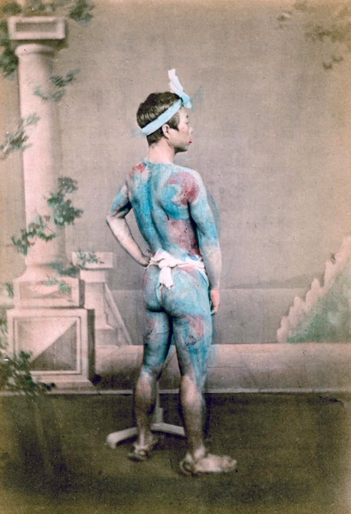 A samurai posing to have his photograph taken, showing off his tattoos
