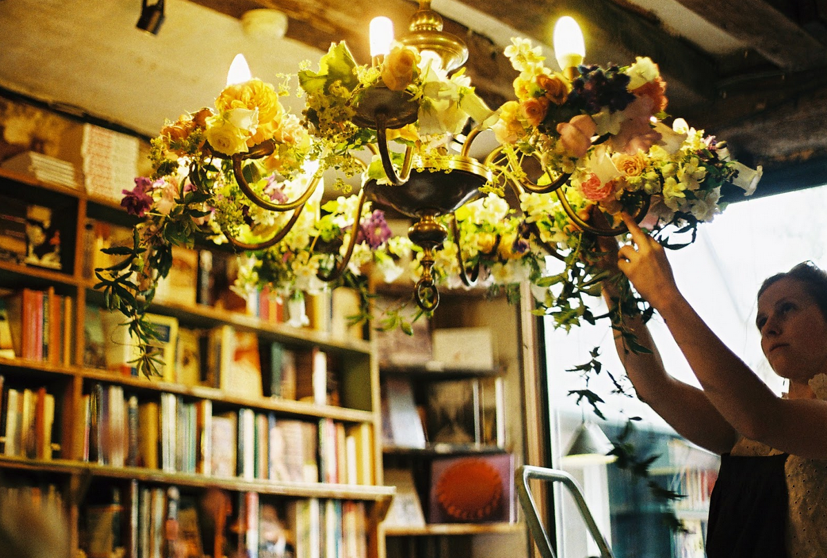 A woman arranging flowers in a chandelier in a library