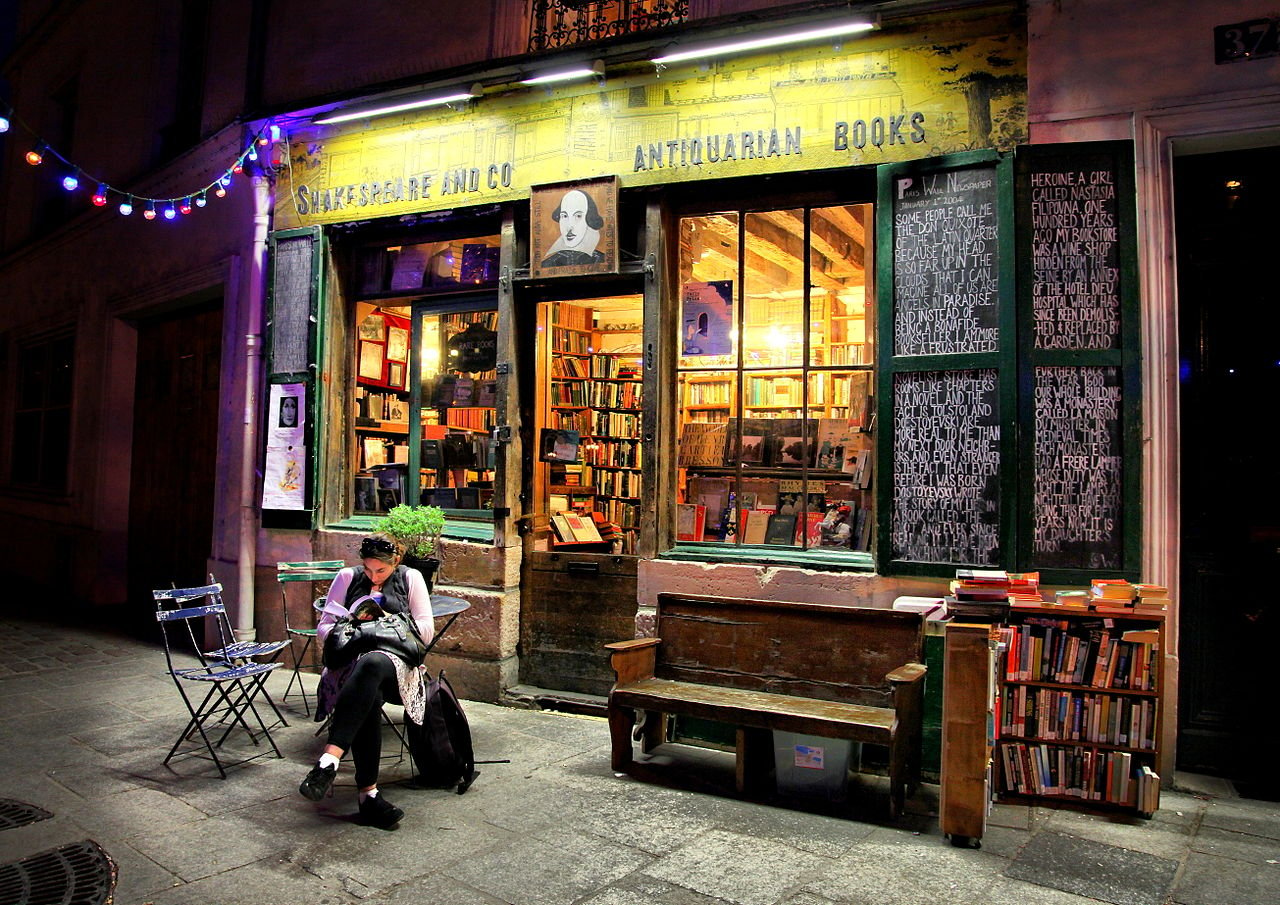 A woman sitting on the patio reading a book outside of a bookstore