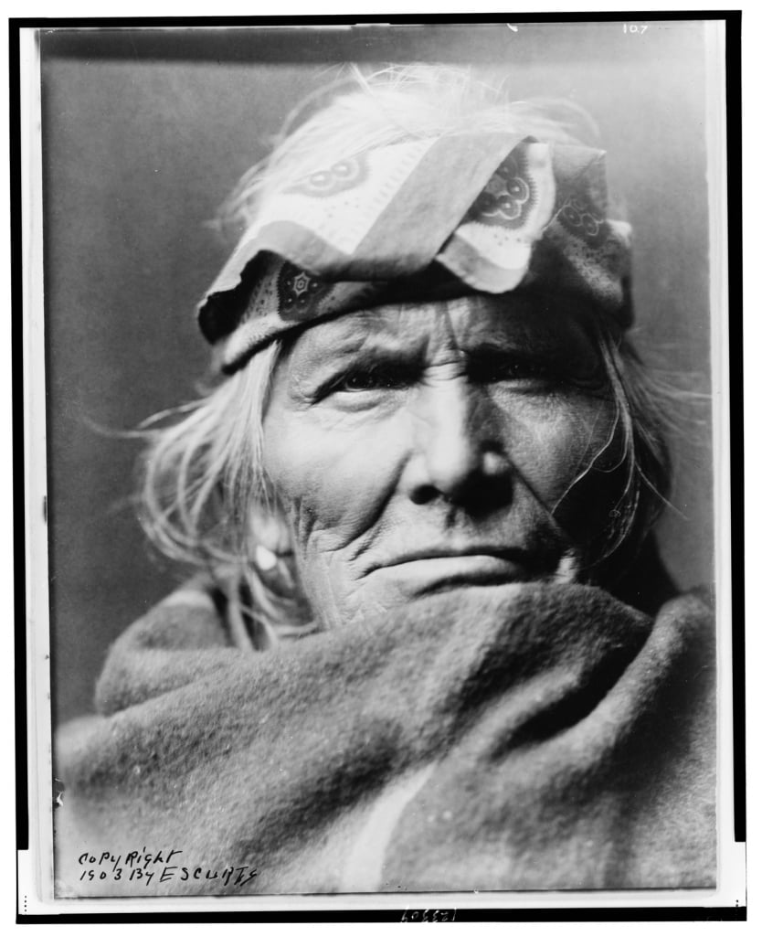Native American with a bandana around his forehead and a large scarf covering his shoulders and neck