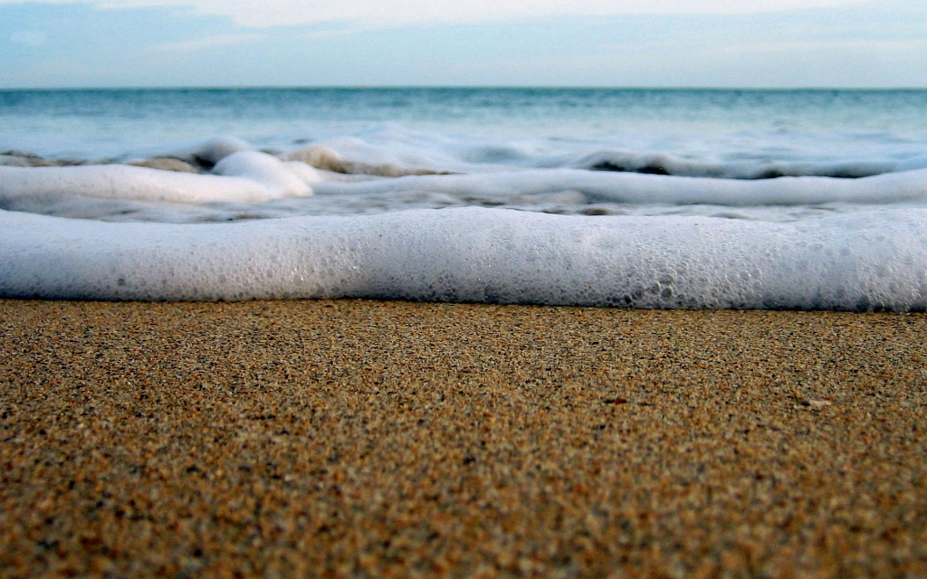 Foamy waves rolling up on a sandy beach.