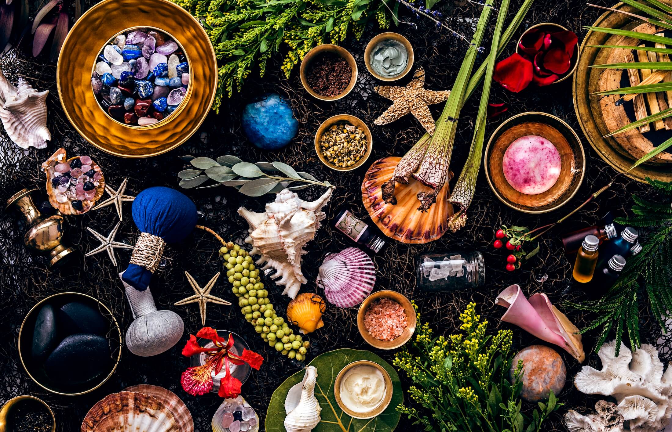 Brass bowls and small dishes of crystals, dried flowers, pink salt, herbs and stones with shells, starfish and small vials.