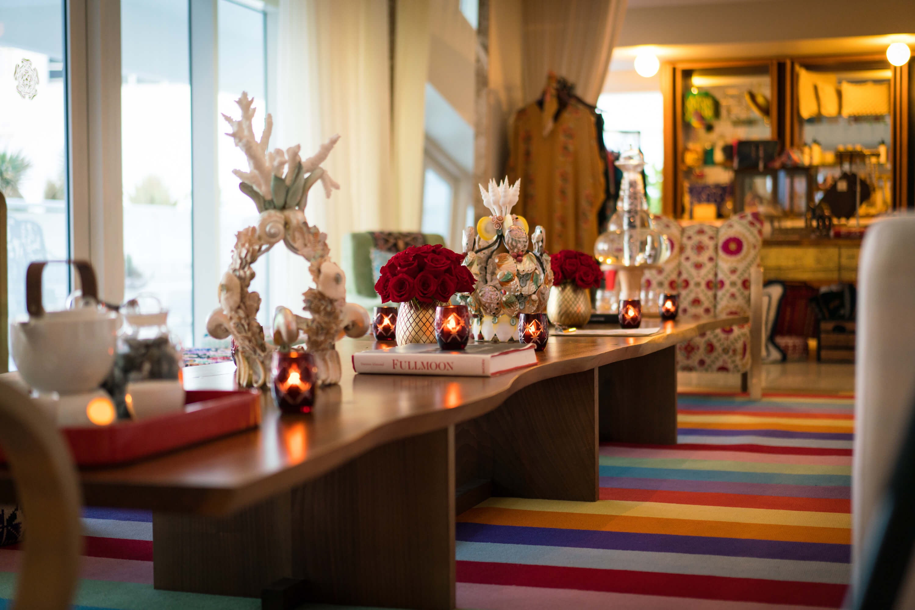 Red roses, a coral-and-shell centerpiece and a tea service sit on a long wooden table over a rainbow-striped carpet in Tierra Santa Healing House.