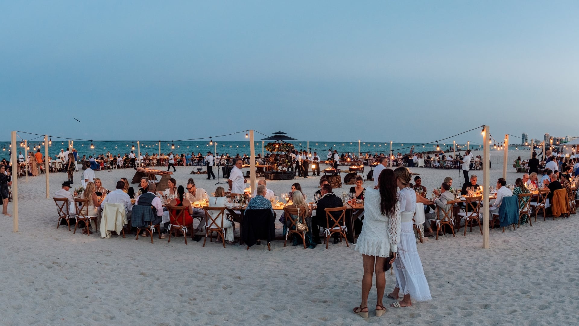 Guests enjoying an elegant beachfront dinner at Faena Beach, with ocean views at sunset.