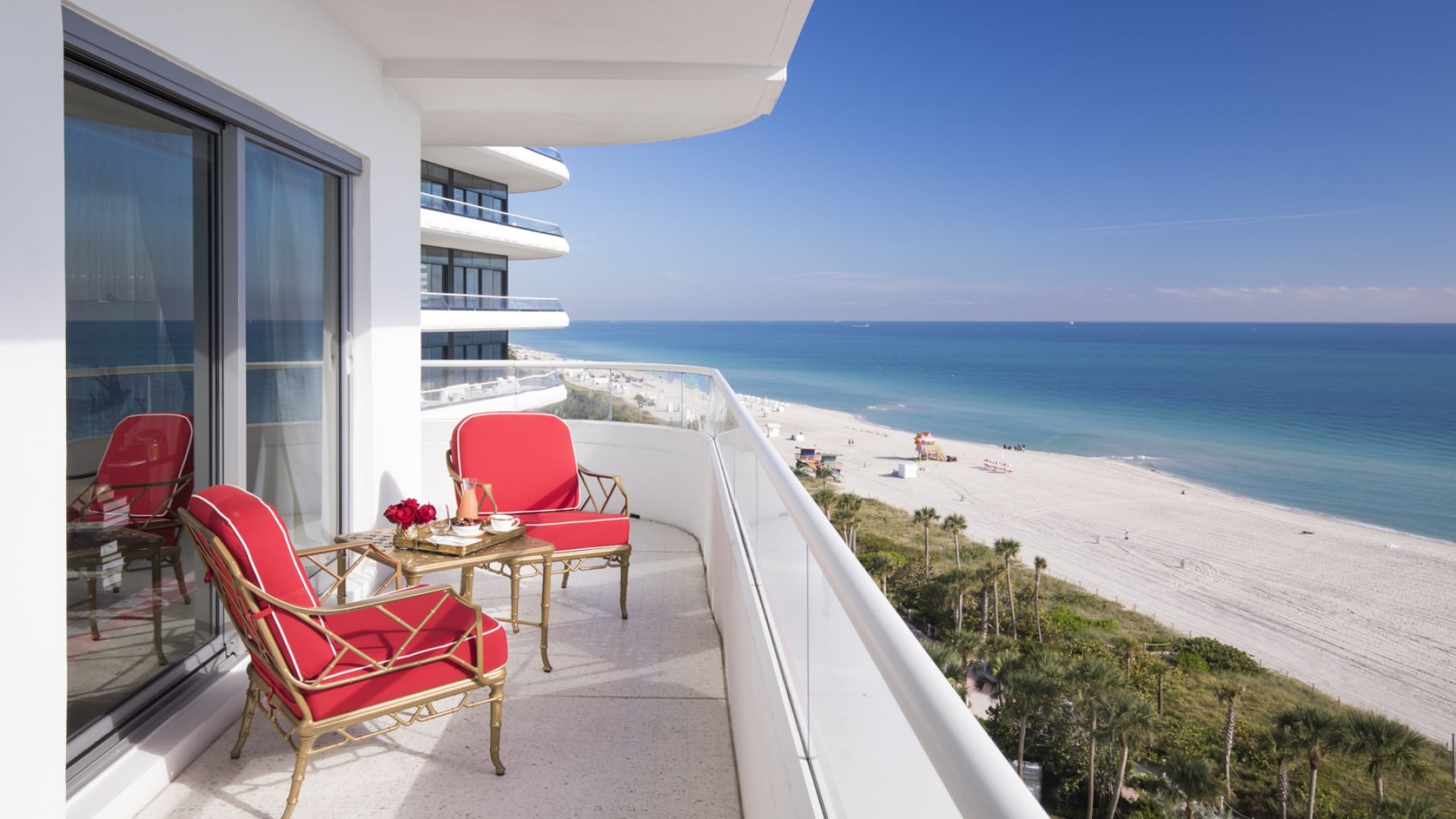 A beachside balcony with red chairs and a table overlooking the ocean.