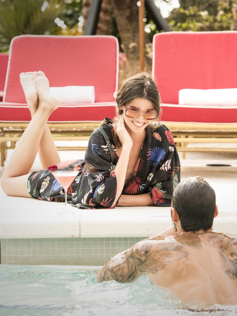 A man and woman enjoying a poolside moment, with the woman lying on the pool edge and the man in the water.