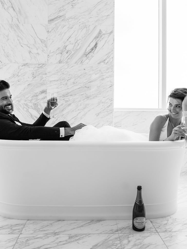 A black and white photo of a couple in a bubble bath with champagne.