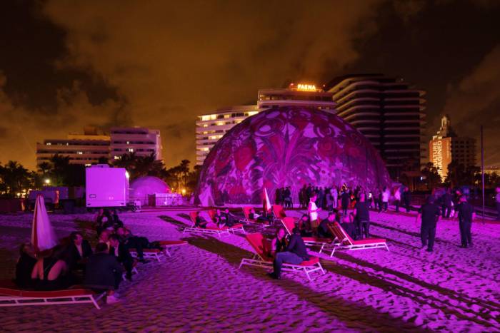 Lit up dome on beach with people socializing