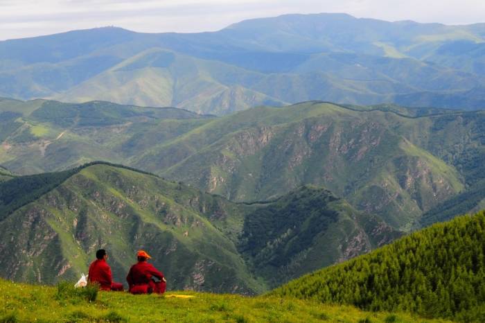 Monks sitting on the top of a hill, looking out over the mountains