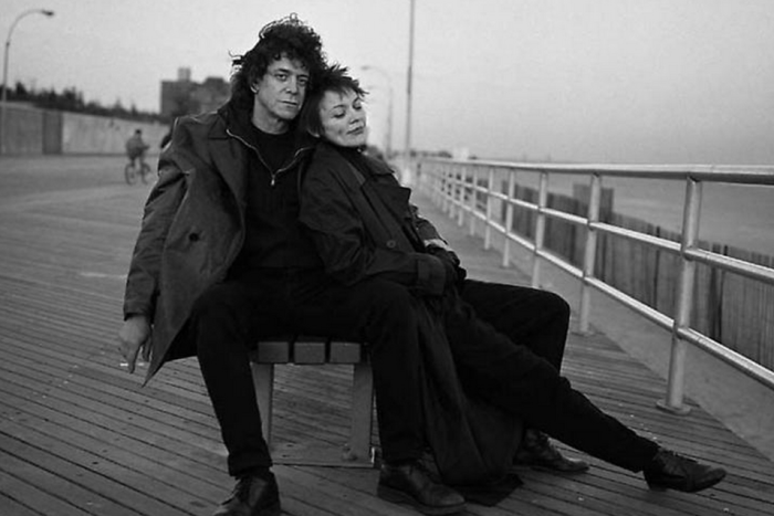 Lou Reed and Laurie Anderson sitting on a bench on a waterfront boardwalk