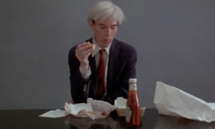 Artist Andy Warhol east a burger and fries. Bottle of ketchup on table.