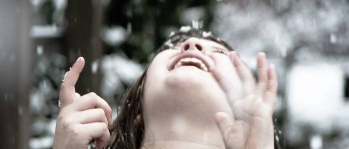 A close up of a child's face looking up to the sky with snow falling on them