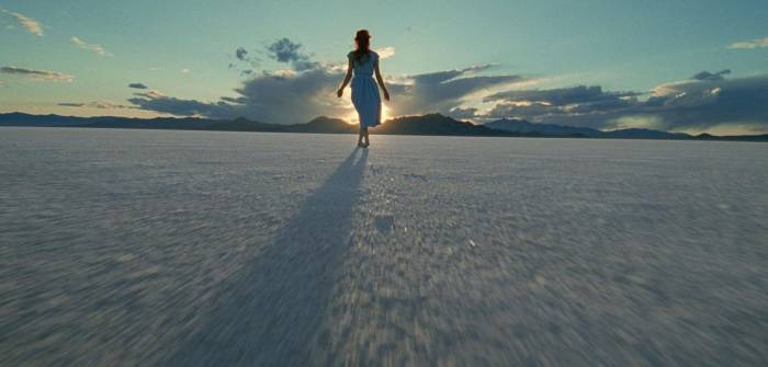 Woman in dress walks on salt flat at sunset.