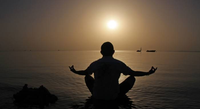 Man meditating on beach at sunset 