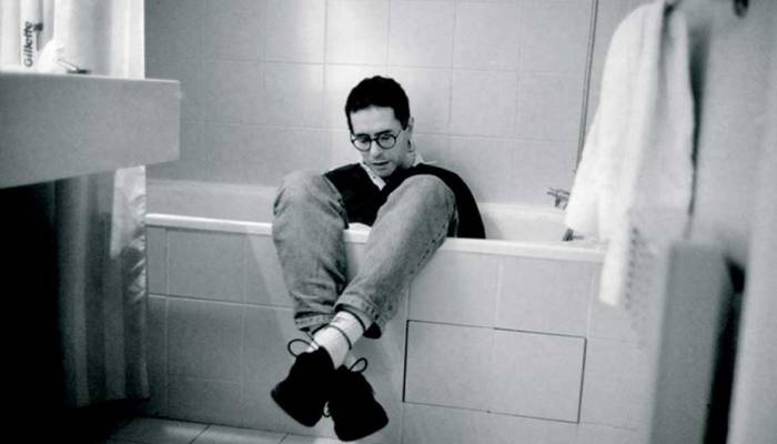 Author Cesar Aira sitting in empty bathtub, clothed.