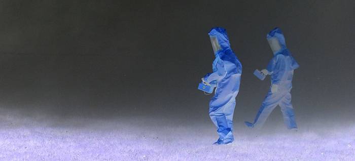 Two people walking in blue hazmat suits.