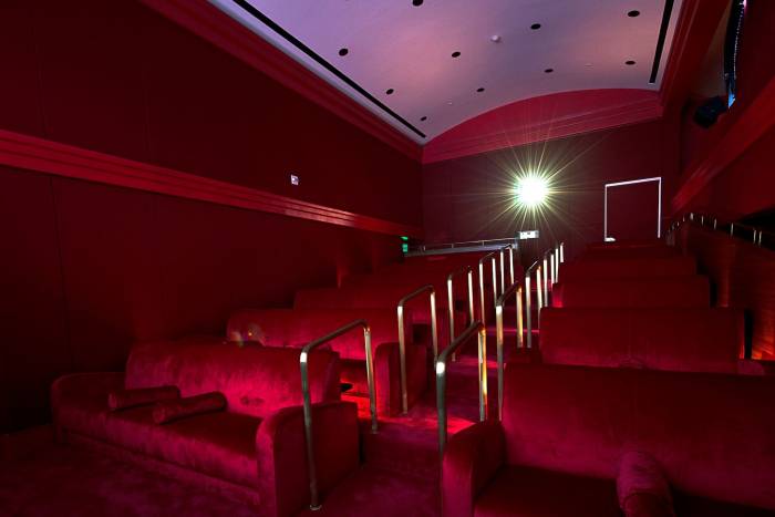 red velvet stairs and movie-theatre style seating with gold handrail with light from projector in background