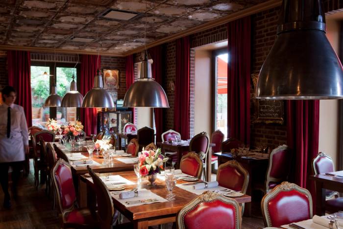 server walks alongside table in room with tin ceiling, large light fixtures, and red chairs framed in gold
