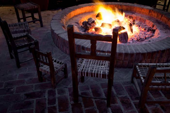 wooden chairs sit around a brick fireplace with small fire burning