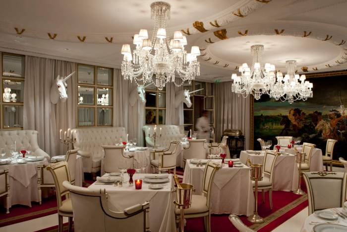 grand dining room with three chandeliers, unicorn heads on walls, red carpet, and white booths, tables, and chairs