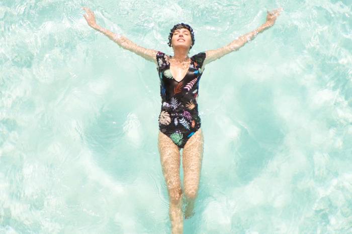 woman in one-piece bathing suit and matching swimcap floats on her back in light blue water