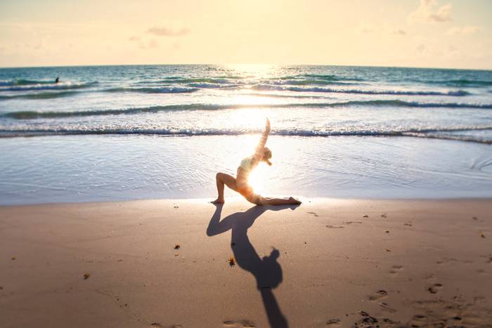 woman performs yoga stretch on beach with sunset in background