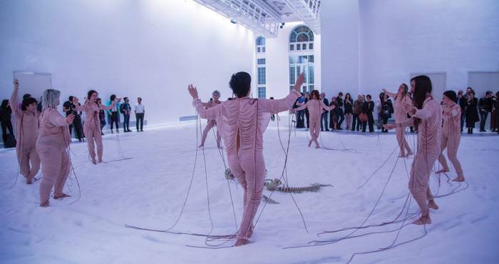 performers dressed in pale pink skin tight fabric dance on white cloth covering the floor
