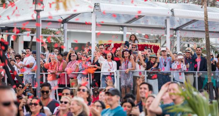 crowd stands along fence while cheering and waving with red confetti in the air