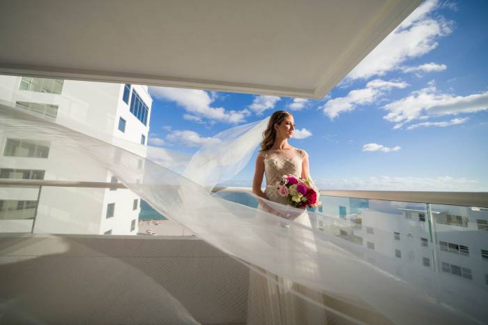 bride stands on balcony with veil flowing in the wind