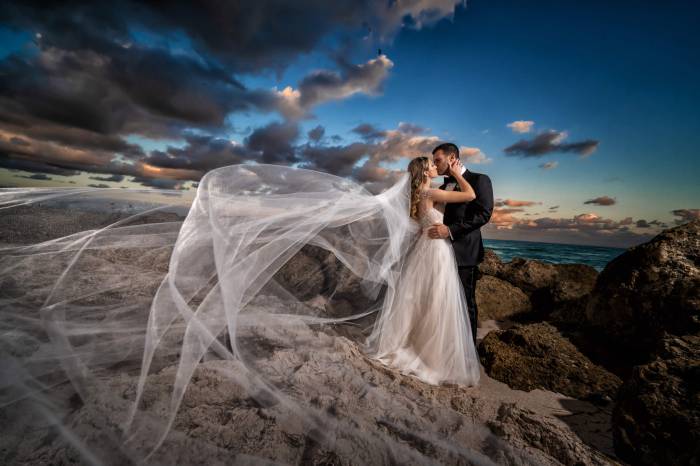 bride and groom kiss on rocks beside the ocean