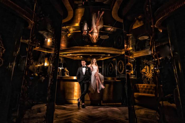 bride and groom sit on a bar in dimly lit room with a golden hue