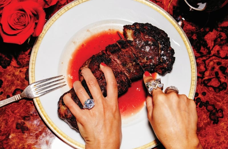A woman in rings holding and cutting a piece of meat