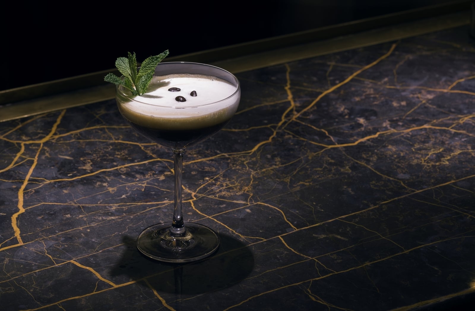 Creamy cocktail garnished with fresh mint and coffee beans on a black marble bar at Faena