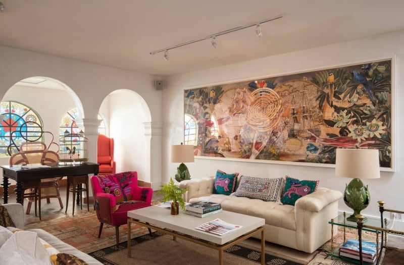 red chair and white couch sit in room with painting on wall and items sitting on side tables