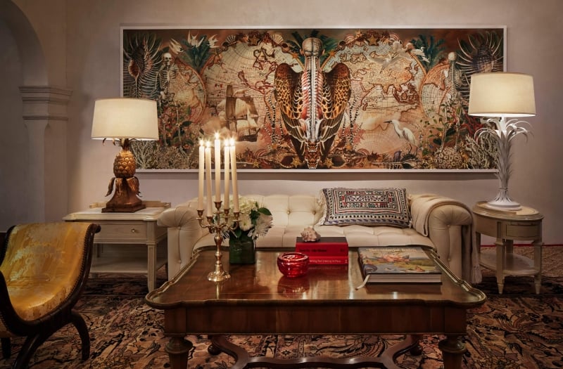 couch and table sit on rug in front of intricate painting and lights