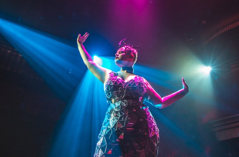 samsara performer in geometric dress holds arms out to their sides